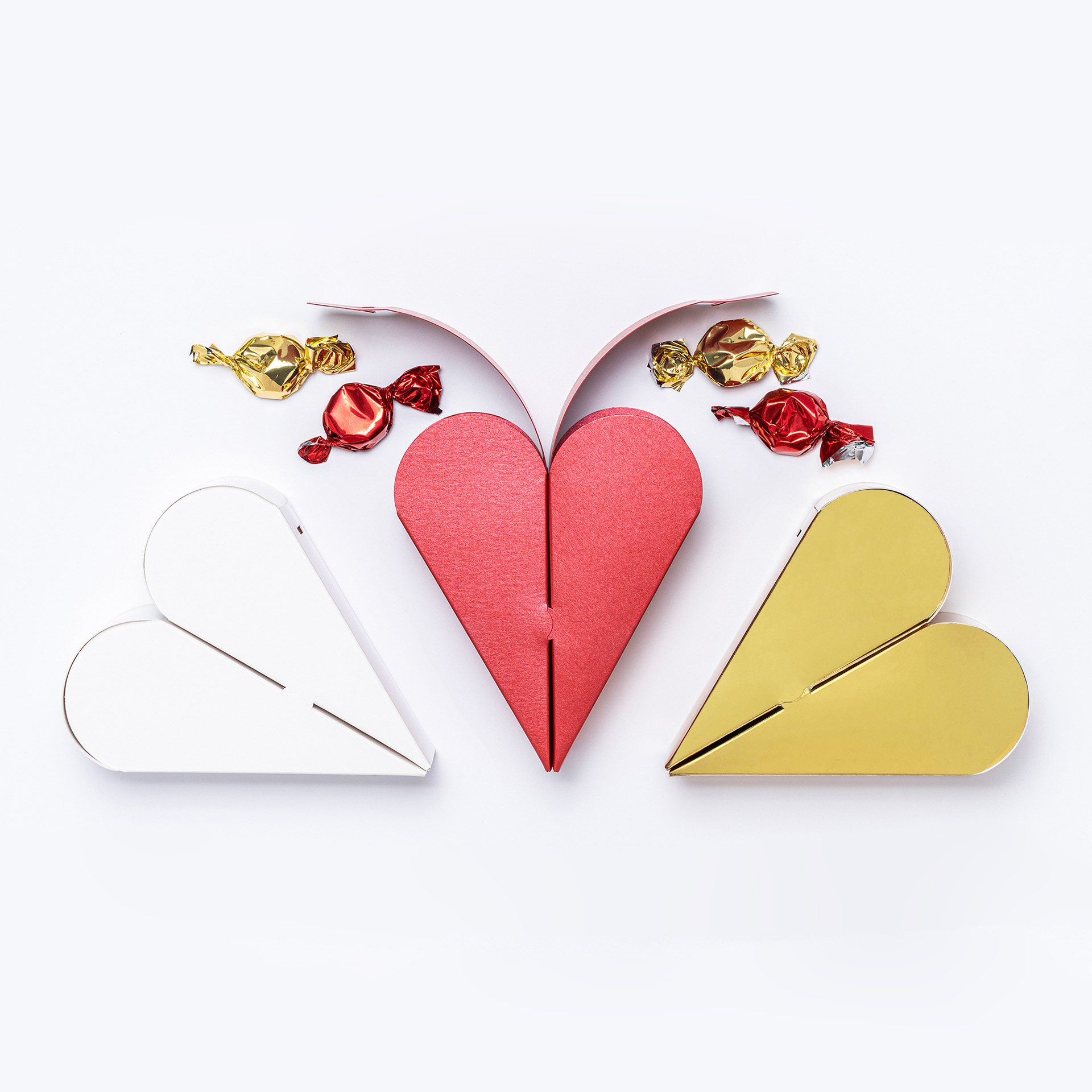 Two part heart gift box in bright gold, pearl red and white. Box open with wrapped sweets falling out