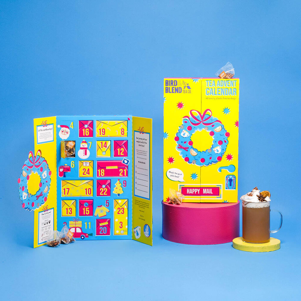 A bespoke 24 Day double door countdown advent 2023 for Bird & Blend Tea. Holds 48 loose tea bags. Yellow, blue and pink festive illustrations and print. On display with a blue background