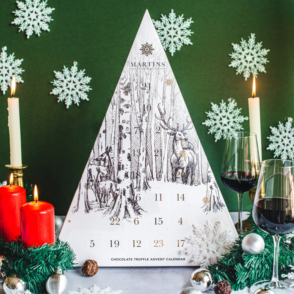 Martins Chocolatier's White Stag Triangle 24 Day Advent Calendar with Bright Gold foil detailed snowflakes & numbers. In a festive winter scene